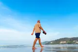 En man med grått hår går i vattenbrynet på en strand