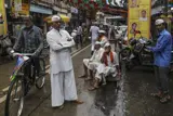 Foto med gatuscen i Mumbai. Till vänster en man på cykel och i mitten flera män som tittar in i kameran.